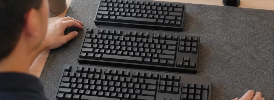 Comparação entre teclados compacto, TKL e tradicional em uma mesa.